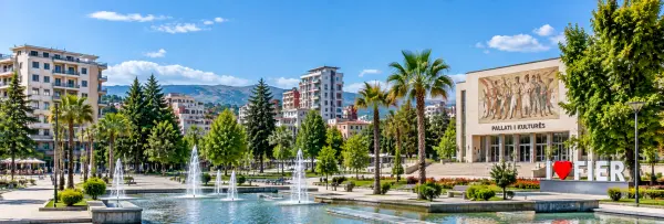 Fier, Albania, with a landscaped city square, fountains, palm trees, cultural center, and surrounding mountains