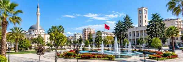Lushnjë, Albania, featuring a mosque, fountains, palm trees, city buildings, and a clock tower