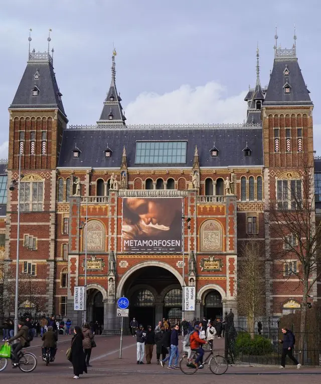 Front entrance of the Rijksmuseum in Amsterdam with visitors and its iconic Gothic Revival architecture.