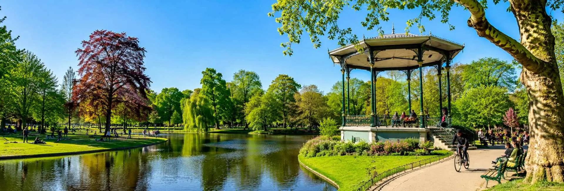 Vondelpark in Amsterdam with a peaceful lake, lush green trees, and the iconic open-air bandstand on a sunny day.