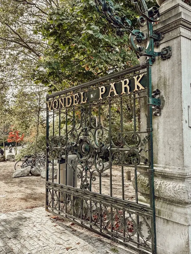 Historic wrought-iron entrance gate of Vondelpark in Amsterdam surrounded by lush trees.