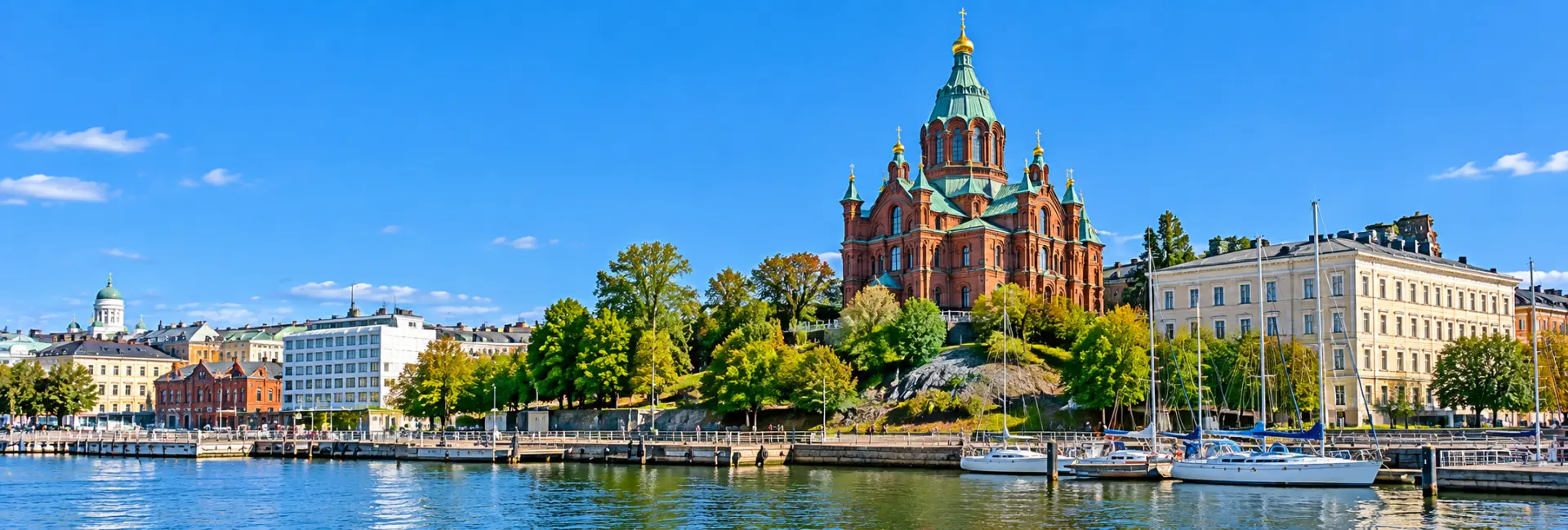 Uspenski Cathedral in Helsinki with red brick walls, green domes, and golden crosses overlooking the harbor.