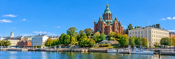 Uspenski Cathedral in Helsinki with red brick walls, green domes, and golden crosses overlooking the harbor.