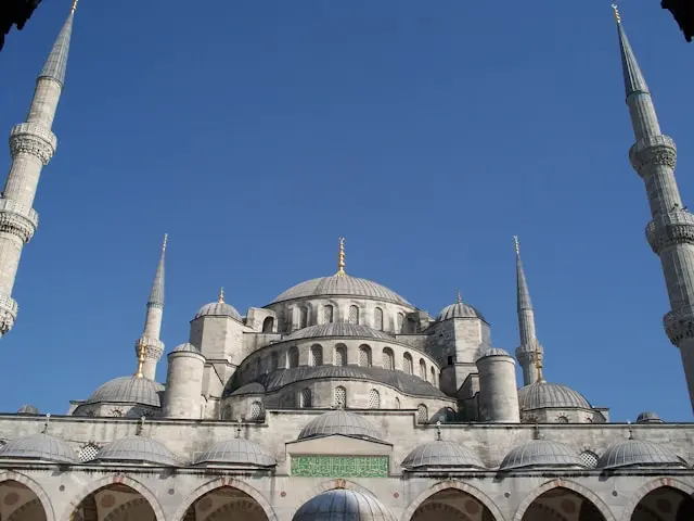 Blue Mosque in Istanbul viewed from the courtyard beneath a clear blue sky.