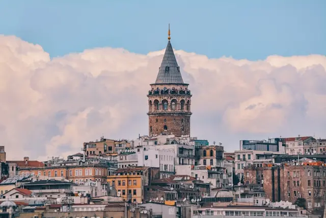 Galata Tower rising above Istanbul’s historic rooftops beneath a cloudy blue sky.
