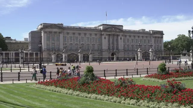Front view of Buckingham Palace with landscaped gardens and visitors on a sunny day in London.