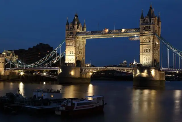 Tower Bridge illuminated at night, with its lights reflected on the River Thames.