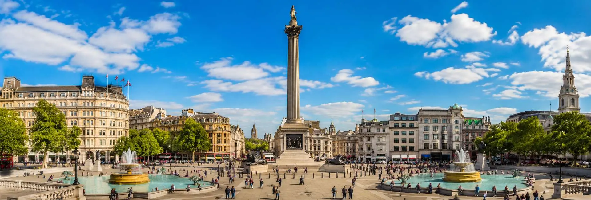 Trafalgar Square in London with Nelson’s Column, fountains, historic buildings and visitors under a blue sky
