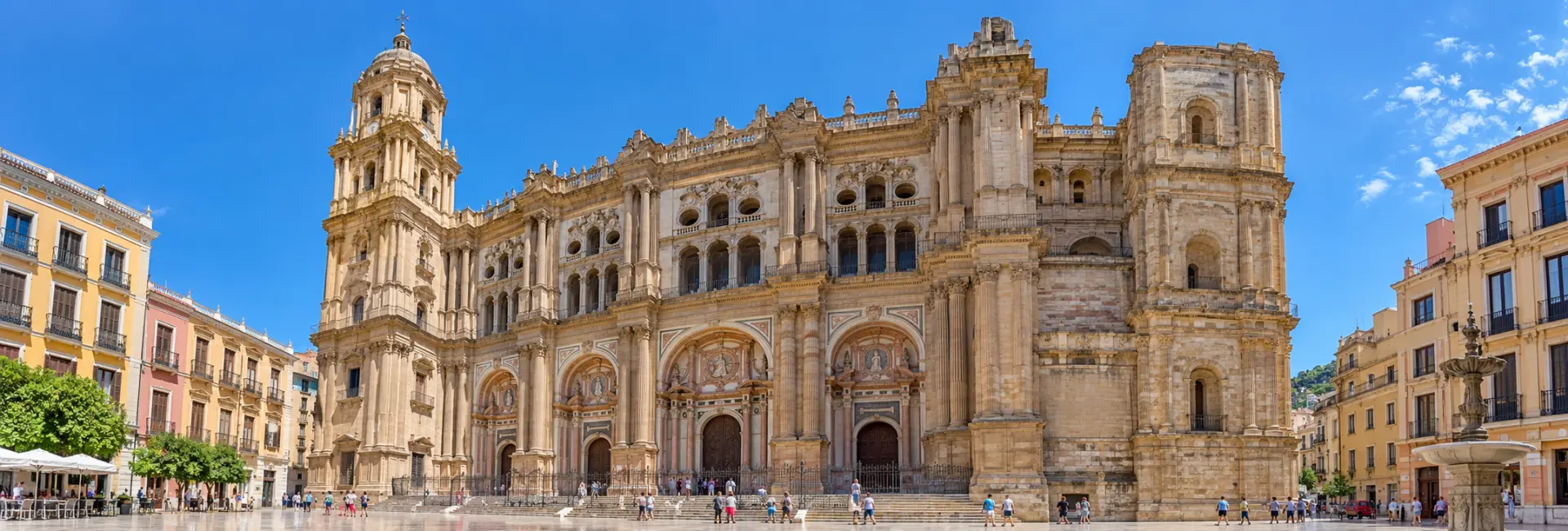 Málaga Cathedral with its ornate stone facade and prominent bell tower beneath a blue sky.