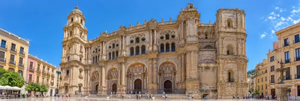 Málaga Cathedral with its ornate stone facade and prominent bell tower beneath a blue sky.