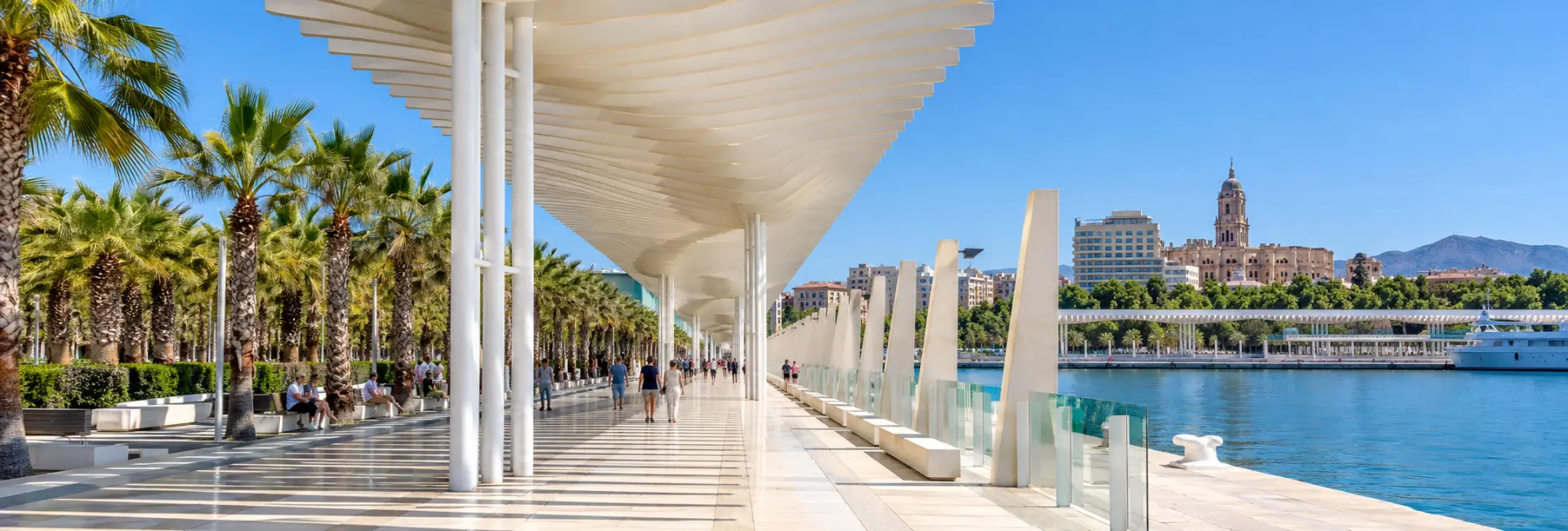 Palmeral de las Sorpresas in Málaga with a white pergola, palms and harbor views.
