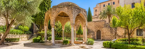 Arab Baths (Banys Àrabs) in Palma de Mallorca, featuring historic stone arches, columns and lush gardens.