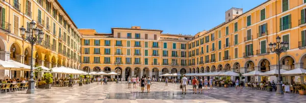 Plaza Mayor in Palma de Mallorca featuring historic buildings, arched walkways and outdoor cafés.