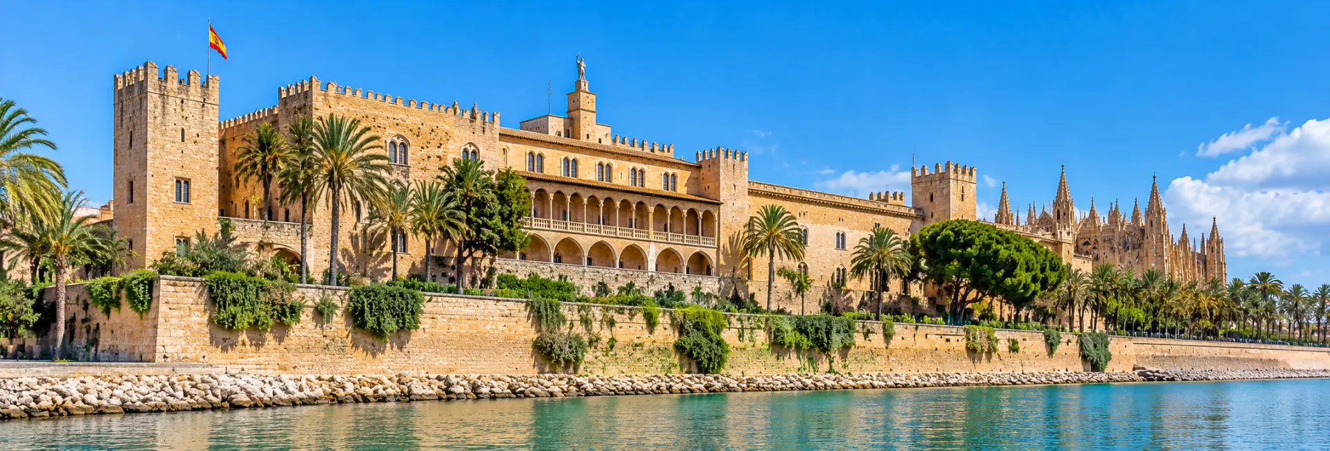 Royal Palace of La Almudaina with historic stone walls and palm trees in Palma de Mallorca, Spain.