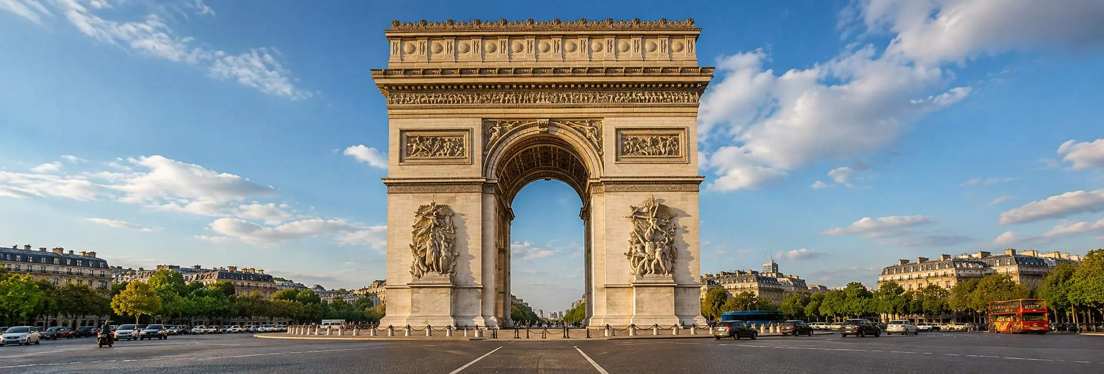 Arc de Triomphe in Paris standing prominently at Place Charles de Gaulle under a bright blue daytime sky.