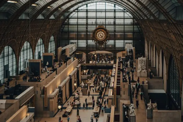 Main exhibition hall of Musée d'Orsay with visitors, sculptures, and the famous central clock.