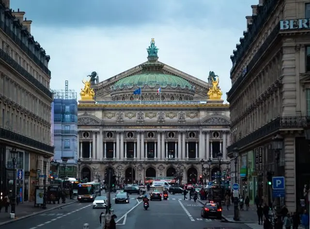 Palais Garnier illuminated at dusk, framed by Parisian streets and historic Haussmann buildings.