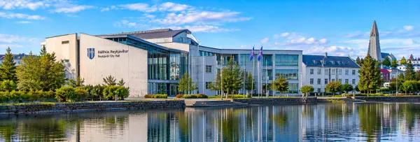 Reykjavík City Hall beside a reflecting pond with Icelandic flags and Hallgrímskirkja