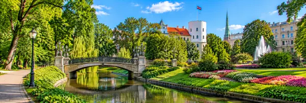 Bastejkalns Park in Riga, Latvia, featuring a scenic canal, pedestrian bridge, colorful flowerbeds and lush greenery.
