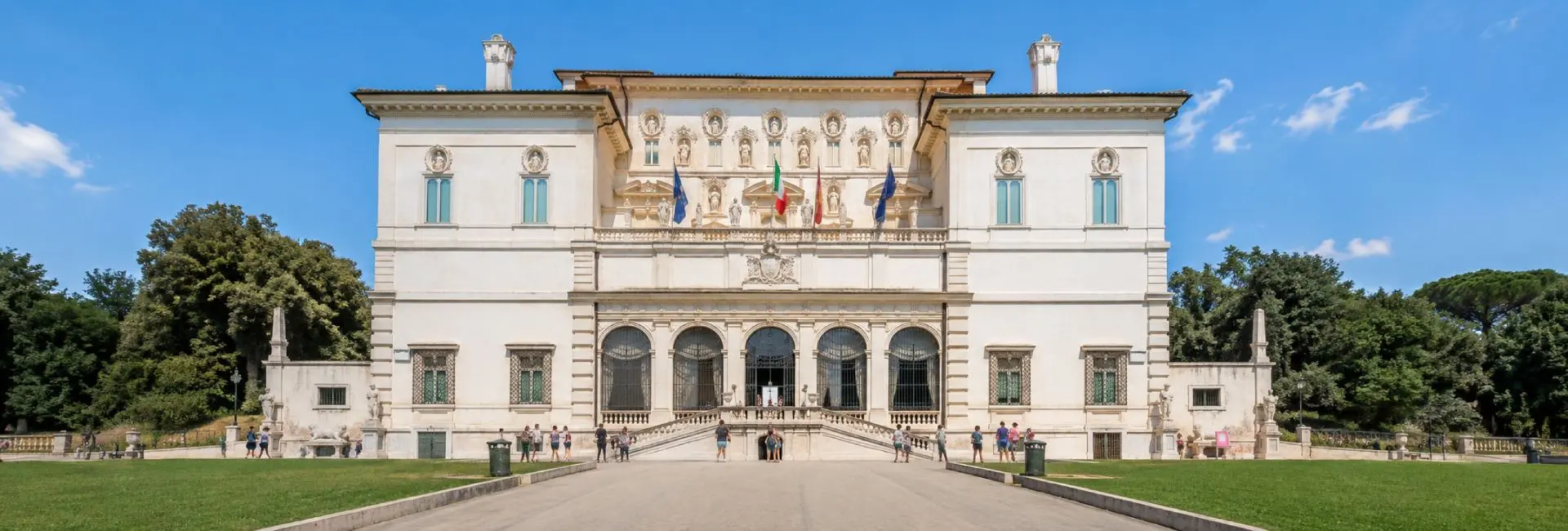 Galleria Borghese museum in Rome with ornate façade, lawns, trees and visitors