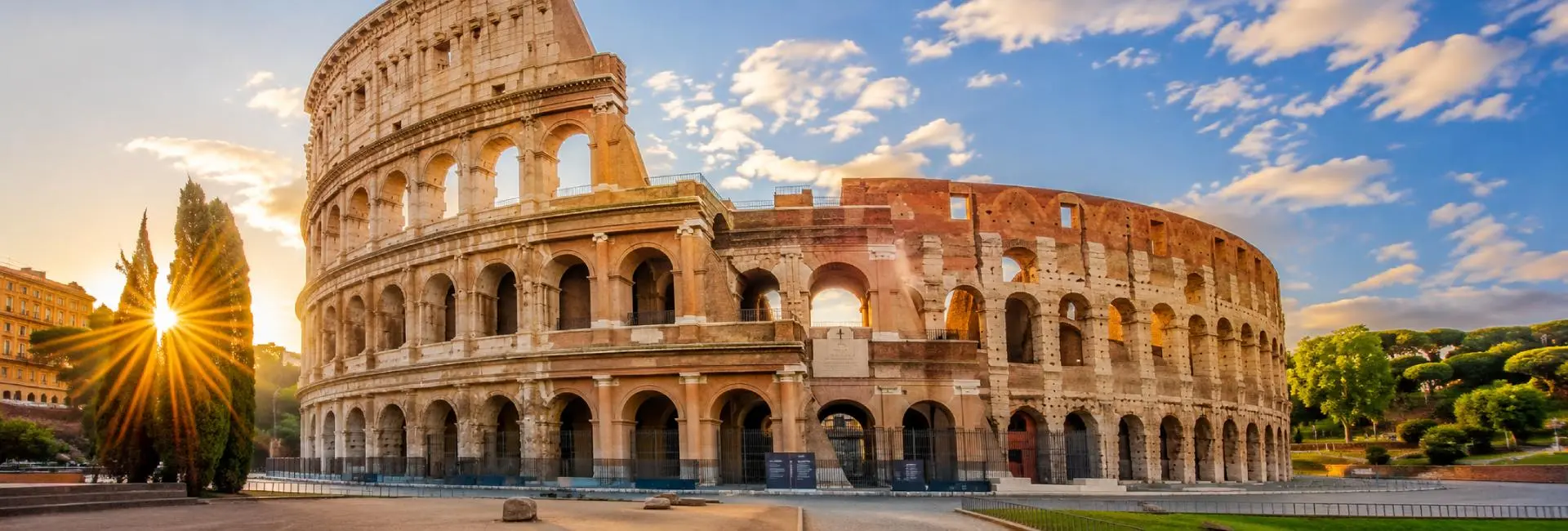 The Colosseum in Rome, Italy, illuminated by warm golden-hour sunlight under a clear blue sky with historic Roman surrou