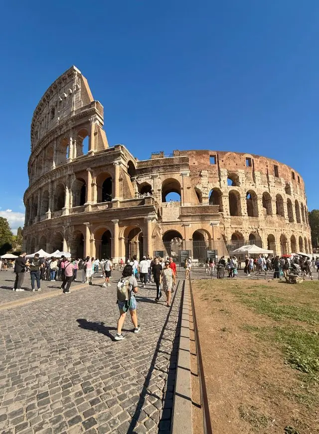 Front view of the Colosseum in Rome, Italy, with visitors walking along the cobblestone path on a sunny day.