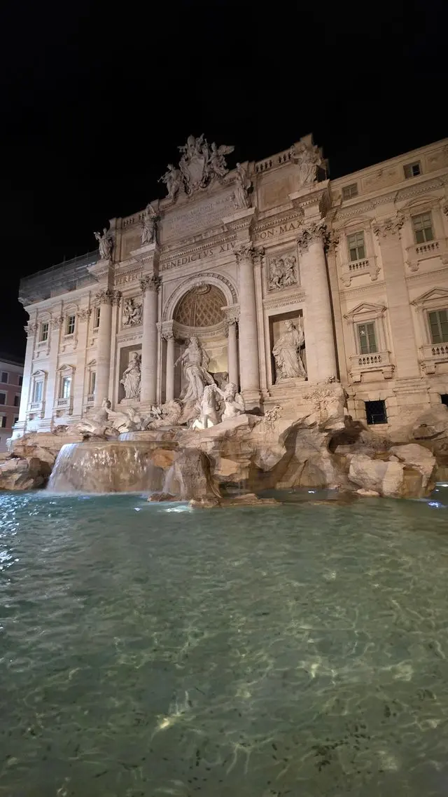 Trevi Fountain illuminated at night with glowing Baroque sculptures and shimmering water in Rome.