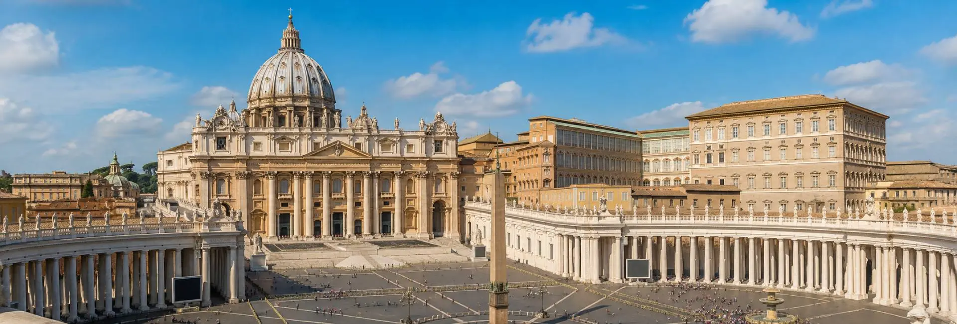 Panoramic daytime view of Vatican City featuring St. Peter's Basilica and St. Peter's Square under a blue sky.