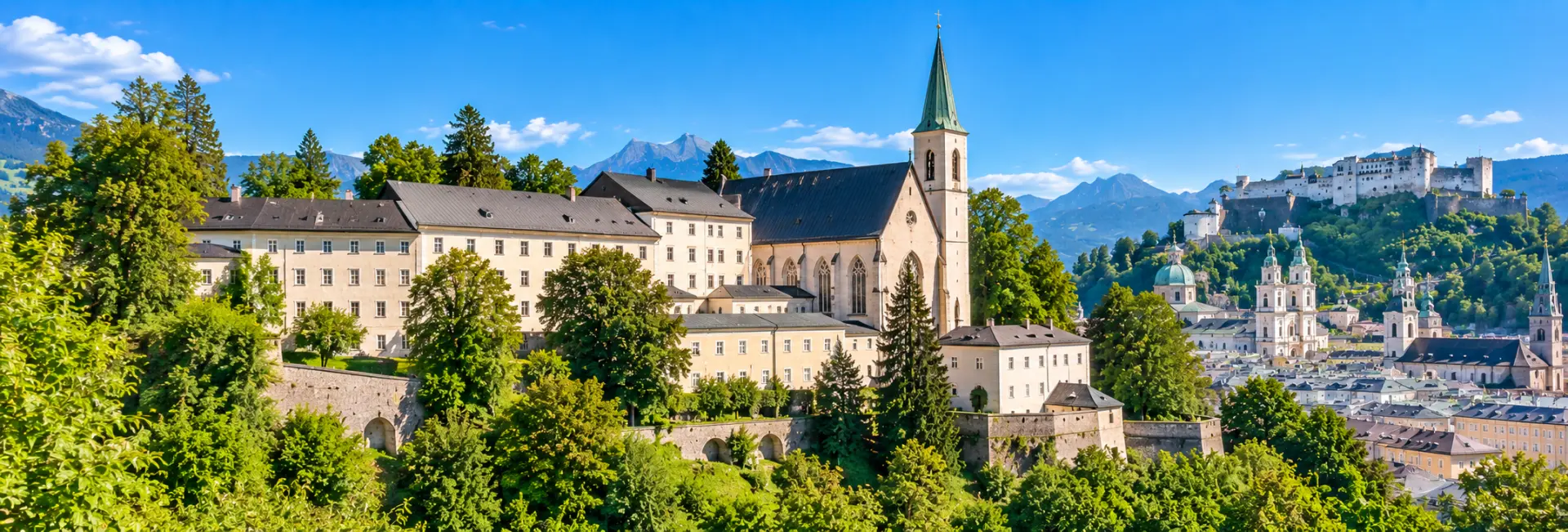 Stift Nonnberg in Salzburg, Austria, surrounded by greenery with the Alps in the background.