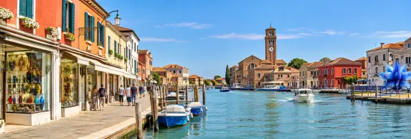 Murano Island, Venice, with colorful waterfront buildings, boats, glass shops, and the historic bell tower.