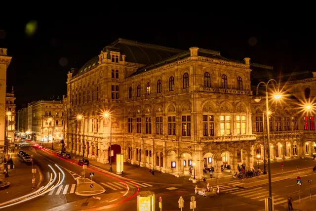 Vienna State Opera illuminated at night with traffic trails on surrounding streets