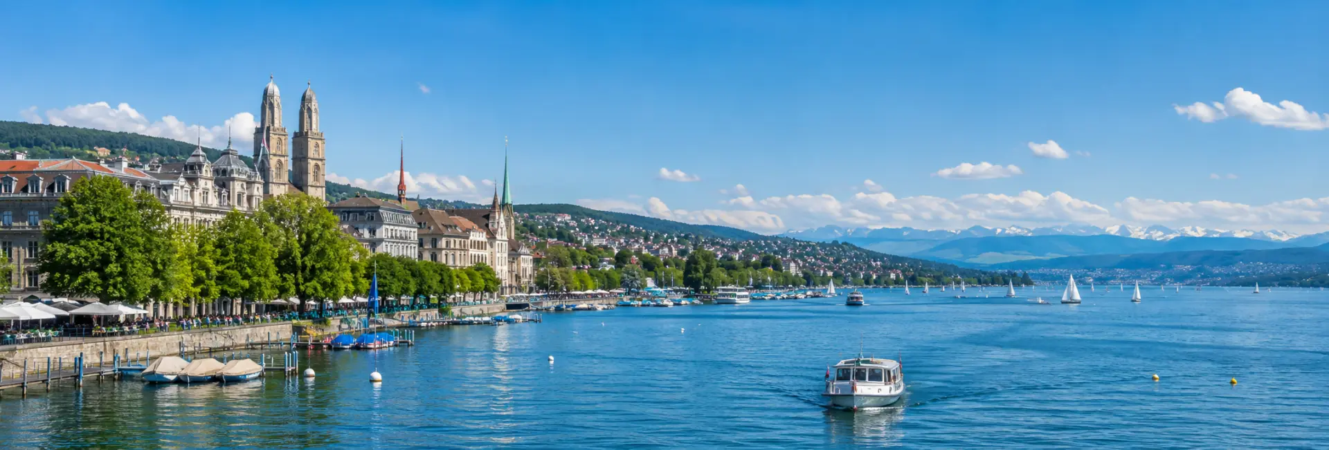 Lake Zurich with sailboats, waterfront promenade, Zurich skyline and distant Swiss Alps