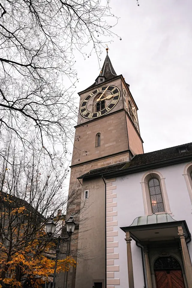 Close-up view of St. Peter’s Church clock tower in Zurich framed by autumn trees