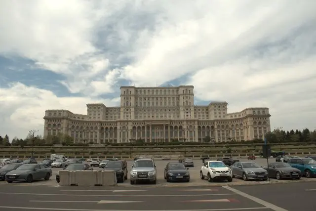 Palace of the Parliament in Bucharest, Romania, featuring an enormous neoclassical facade beneath a cloudy sky.