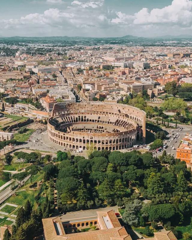 Aerial view of the Colosseum surrounded by parks and historic buildings in Rome.