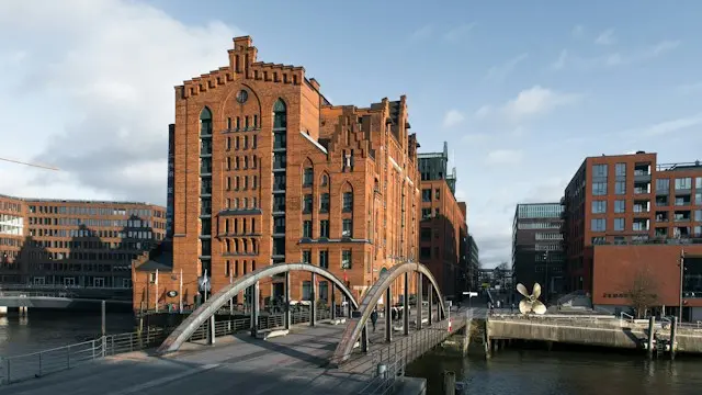 Historic red-brick warehouses and a modern arched bridge along Hamburg's waterfront.