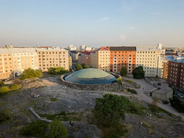Circular pavilion surrounded by colourful historic buildings in a public square in Helsinki, Finland.