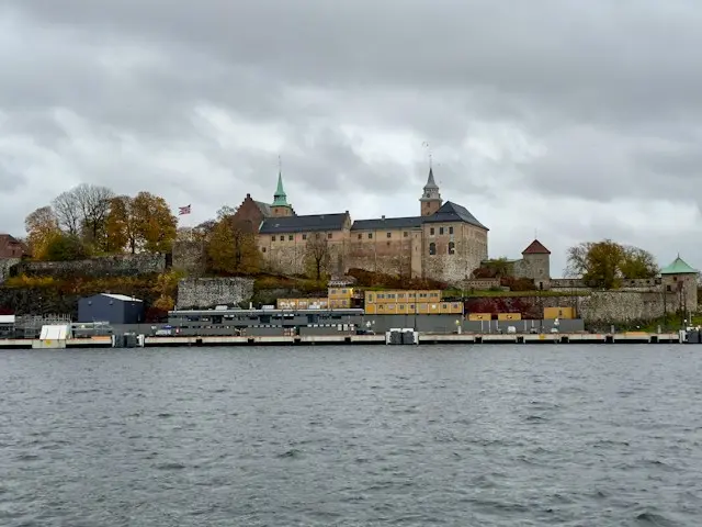 Akershus Fortress overlooking Oslo's waterfront, with historic stone buildings and autumn trees.
