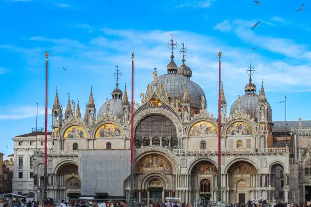 Ornate St. Mark’s Basilica overlooking St. Mark’s Square in Venice under a blue sky.