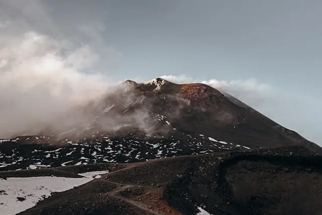 Mount Etna volcano in Sicily with snow-covered slopes and drifting clouds.