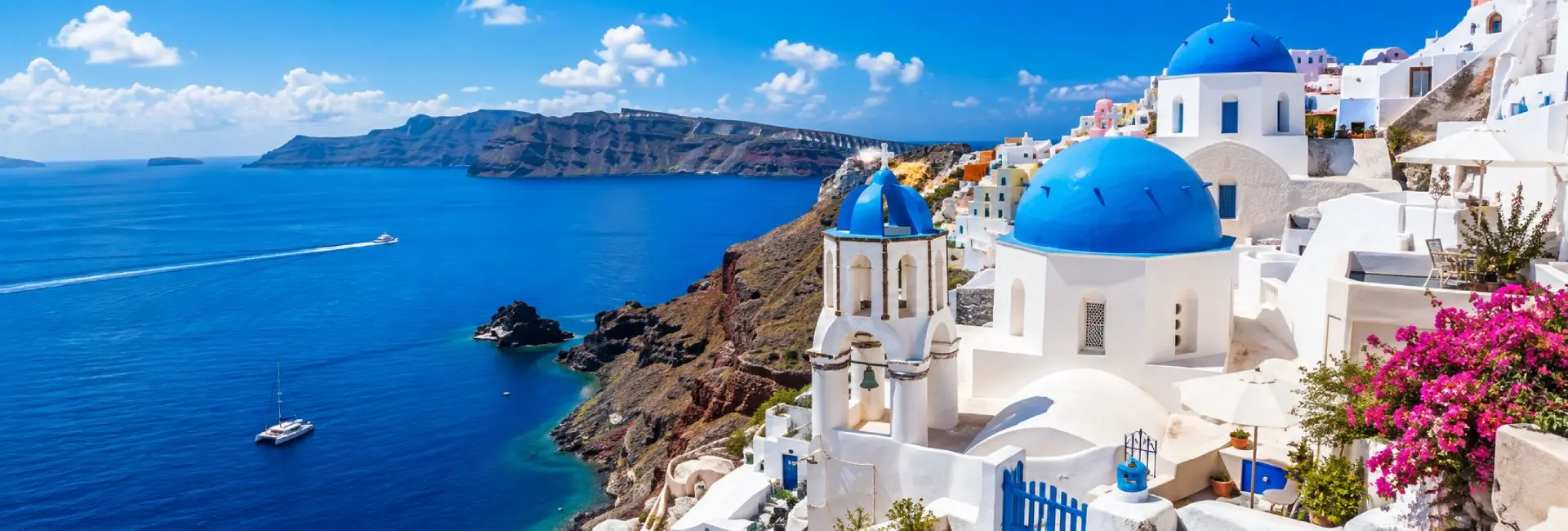 Panoramic summer view of Santorini, Greece, featuring iconic whitewashed buildings with blue-domed churches overlooking