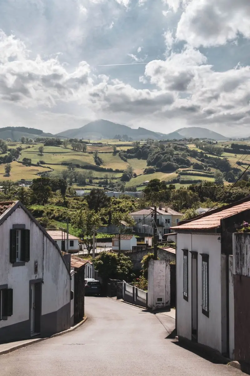 Scenic countryside road with rolling green hills and traditional houses in the Azores, Portugal