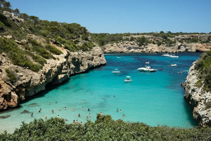 Turquoise Cala beach surrounded by rocky cliffs and boats in Mallorca, Spain