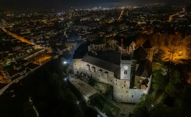 Aerial night view of Ljubljana Castle in Slovenia, featuring illuminated medieval walls and the surrounding city skyline