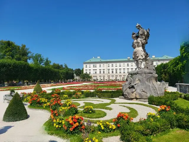 Colorful flower gardens, Pegasus Fountain and Mirabell Palace under a clear blue sky in Salzburg, Austria.