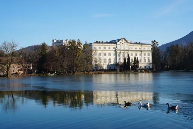 Leopoldskron Palace overlooking a peaceful lake with swans and mountain scenery in Salzburg, Austria.