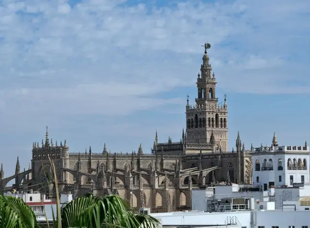 Historic Gothic architecture and ornate bell tower in Seville, Spain, beneath a blue sky.