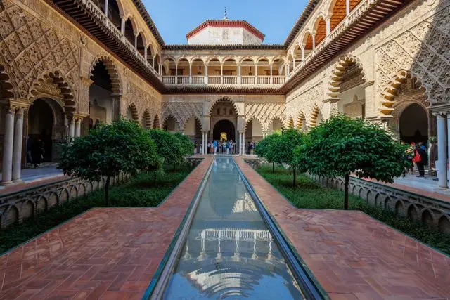 Traditional Andalusian courtyard in Seville with a reflecting pool, arches and manicured gardens.