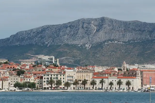 Panoramic view of Split, Croatia, featuring historic red-roofed buildings, a waterfront promenade, and mountains.