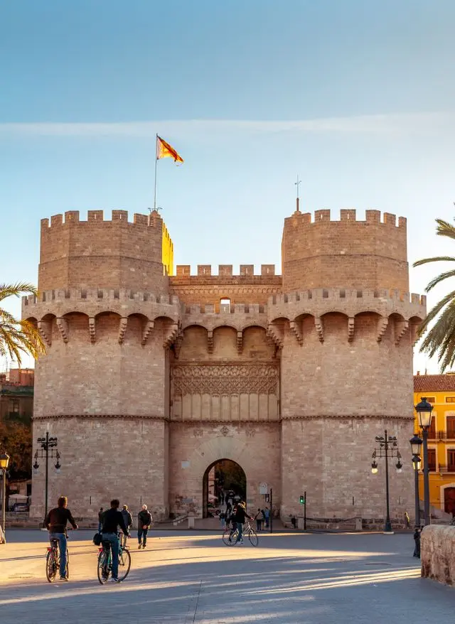 Torres de Serranos, Valencia, Spain, with historic stone towers and cyclists in the foreground.